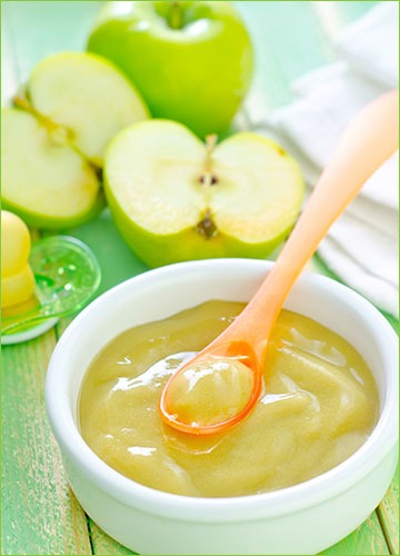 Applesauce in a dish with apples around it